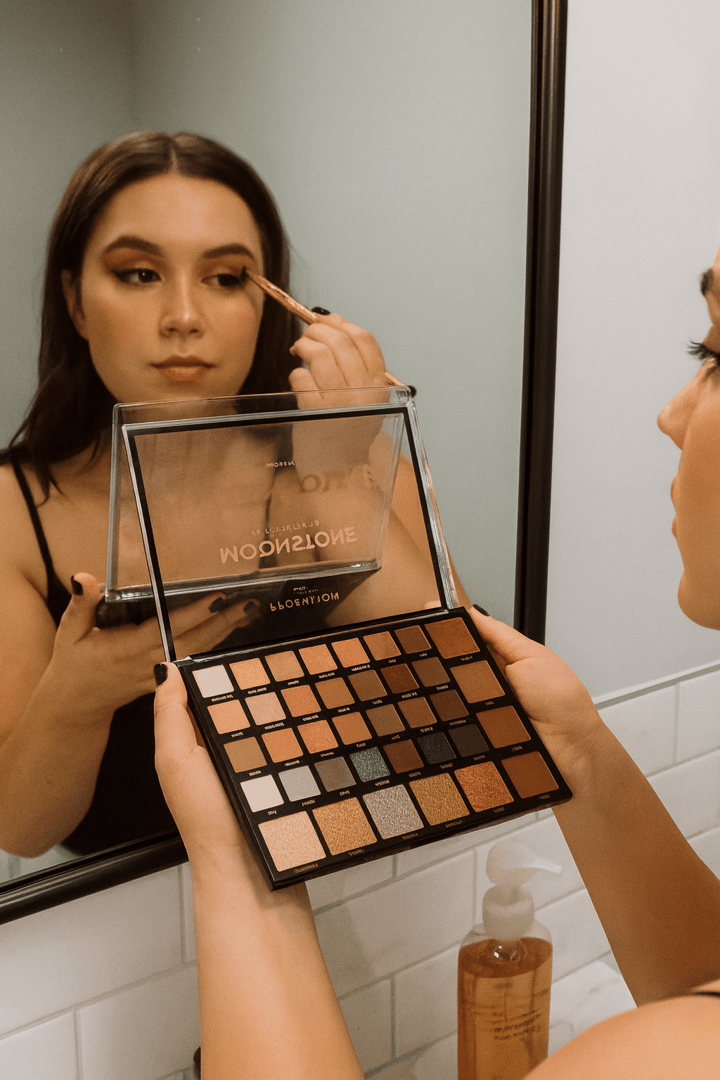 Profusion Cosmetics Moonstone 42 shade eyeshadow palette with matte and shimmer finishes held by woman applying makeup in front of mirror